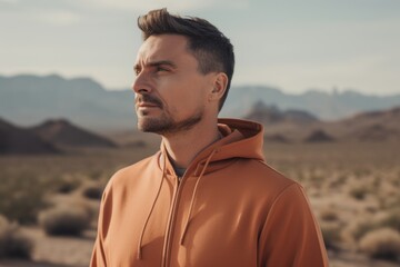 Handsome young man in orange hoodie walking in the desert