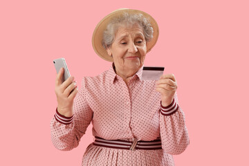 Senior woman with mobile phone and credit card on pink background