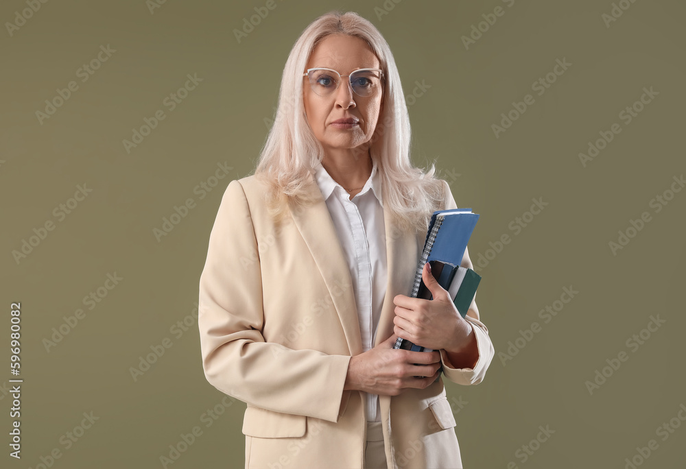 Mature teacher with notebooks on green background