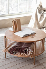 Books, glasses and folded blanket on coffee table in interior of cozy living room