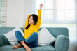 © sorapop - Happy woman stretch oneself for relaxing activity feeling lazy on weekend on couch, resting napping break, Lifestyle Asian young female stretching her arms on sofa in the living room at home
