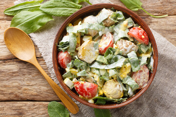 Wall Mural - Homemade salad of boiled eggs, potatoes, tomatoes, onions and sorrel, spinach with cream dressing close-up in a bowl on a wooden table. Horizontal top view from above