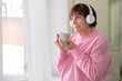 Elderly woman in pink, sipping coffee and listening to music - contentment personified