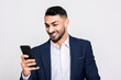 © ABCreative - Cheerful attractive turkish man in smart suit holding new modern cellphone smartphone observing photos i phone chatting messaging with friends family girlfriend.