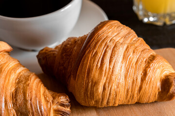 Coffee cup with croissant on a rustic dark wooden table. Food series. Two tasty fresh croissants, jam, orange juice. Continental breakfast served with freshly baked pastry. Close up view, Good morning