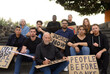 © Gabriel Trujillo - Group of determined diverse protesters in casual clothes sitting on stairs with carton placards and looking at camera before demonstration
