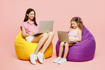 Wall Mural - Full body IT woman wear casual clothes with child kid girl 6-7 years old. Mother daughter sit in bag chair work hold use laptop pc computer isolated on plain pink background Family parent day concept