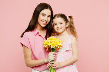 Wall Mural - Happy fun woman wear casual clothes with child kid girl 6-7 years old. Mother daughter hold bouquet of daffodil flowers, hug, cuddle isolated on plain pastel pink background Family parent day concept