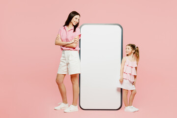 Wall Mural - Full body sideways woman in casual clothes with child kid girl 6-7 years old. Mother daughter big huge blank screen area mobile cell phone isolated on plain pink background Family parent day concept