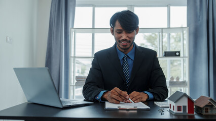 Wall Mural - Mixed race asian indian man realtor chinese people with house model in formal suit in office at desk workplace.