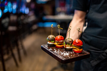 Waiter hold set mini hamburgers, mini burgers on plate in restaurant