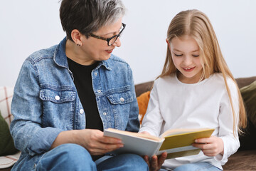 Grandmother and daughter read a book at home on Sofa.