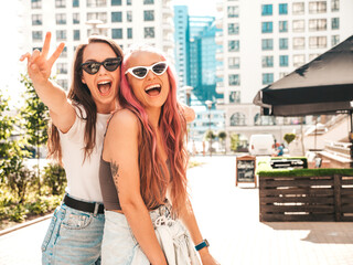 Wall Mural - Two young beautiful smiling hipster female in trendy summer clothes. Sexy carefree women posing in the street. Positive pure models having fun at sunset, hugging and going crazy. In sunglasses