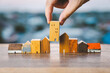 © sommart - Hand choosing mini wood house model from model on wood table, selective focus, Planning to buy property. Choose what's the best. A symbol for construction ,ecology, loan concepts