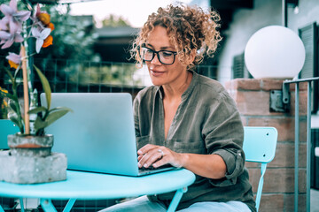 One modern happy serene woman using computer outdoor at home in garden. Pretty female writing on laptop outside house. Alternative workplace and wireless connection technology. People with notebook