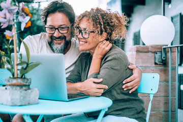 Modern couple enjoying video call on laptop sitting outside home in the garden. Wireless connection. People man and woman using computer outdoor enjoying time and love. Man embracing woman bonding