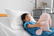 cheerful asian girl in hospital gown lying on bed in clinic and playing with toy bunny.