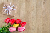 Fototapeta Tulipany - A bouquet of bright colorful tulips and a gift box on a wooden background. Copy space