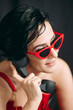Fashionable young lady with red glasses talking on telephone in front of black background