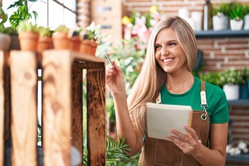 Wall Mural - Young blonde woman florist smiling confident writing on notebook at flower shop