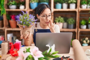 Canvas Print - Young hispanic woman working at florist shop doing video call hand on mouth telling secret rumor, whispering malicious talk conversation