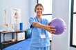 © Krakenimages.com - Young hispanic woman physiotherapist stretching arms using ball at rehab clinic