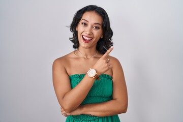 Sticker - Young hispanic woman standing over isolated background with a big smile on face, pointing with hand finger to the side looking at the camera.