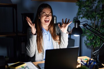 Poster - Young brunette woman working at the office at night celebrating mad and crazy for success with arms raised and closed eyes screaming excited. winner concept