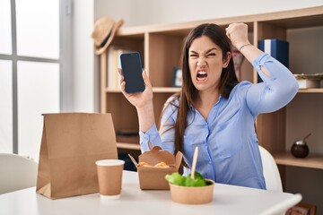 Sticker - Young brunette woman eating take away food at home showing smartphone screen annoyed and frustrated shouting with anger, yelling crazy with anger and hand raised