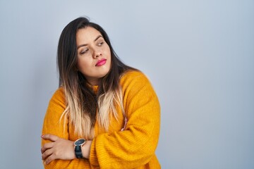 Wall Mural - Young hispanic woman standing over isolated background looking to the side with arms crossed convinced and confident