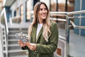 Wall Mural - Young woman smiling confident holding dollars at street