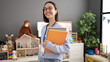 © Krakenimages.com - Young beautiful hispanic woman teacher smiling confident holding books at kindergarten