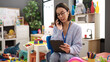 © Krakenimages.com - Young beautiful hispanic woman working as a teacher talking on smartphone using touchpad at kindergarten