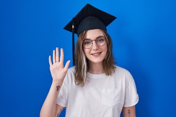 Sticker - Blonde caucasian woman wearing graduation cap showing and pointing up with fingers number five while smiling confident and happy.