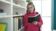 © Krakenimages.com - Young blonde woman student reading book standing at library university