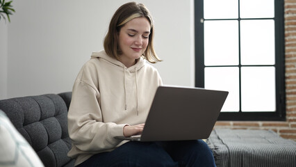 Poster - Young blonde woman using laptop sitting on sofa at home