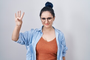 Wall Mural - Young modern girl with blue hair standing over white background showing and pointing up with fingers number four while smiling confident and happy.