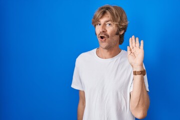 Canvas Print - Middle age man standing over blue background waiving saying hello happy and smiling, friendly welcome gesture