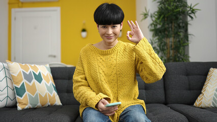 Poster - Young chinese woman using smartphone doing ok gesture with fingers at home