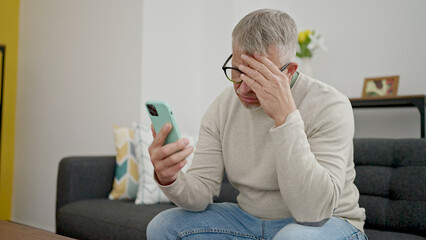 Wall Mural - Middle age grey-haired man using smartphone with stressed expression at home