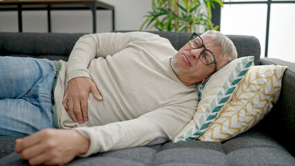 Poster - Middle age grey-haired man suffering for stomach ache lying on sofa at home