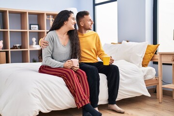 Poster - Man and woman couple drinking coffee sitting on bed at bedroom