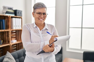 Poster - Middle age woman psychologist writing on clipboard standing at pyschology center