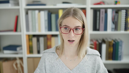 Sticker - Young blonde woman sitting with surprised expression at library university