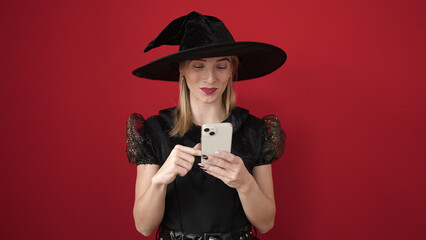 Canvas Print - Young blonde woman wearing witch costume using smartphone over isolated red background