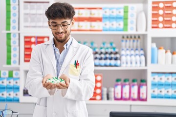 Wall Mural - Young arab man pharmacist smiling confident holding capsules at pharmacy