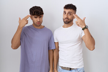 Poster - Homosexual gay couple standing over white background shooting and killing oneself pointing hand and fingers to head like gun, suicide gesture.