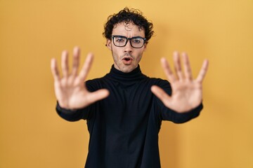 Poster - Hispanic man standing over yellow background doing stop gesture with hands palms, angry and frustration expression