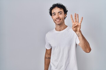 Wall Mural - Hispanic man standing over isolated background showing and pointing up with fingers number four while smiling confident and happy.