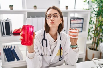 Sticker - Young caucasian dentist woman holding denture and mouthwash looking at the camera blowing a kiss being lovely and sexy. love expression.